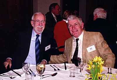 Two men sitting at a dining table with bottles of wine.